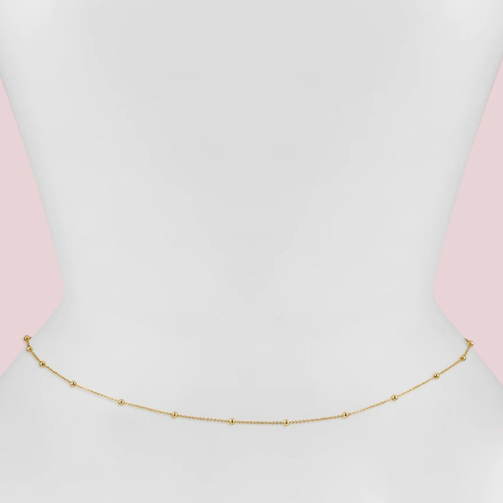 Gold necklace on a person wearing a pink top with a light gray background