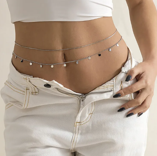 Person wearing a thin silver chain belt with small beads on a plain background