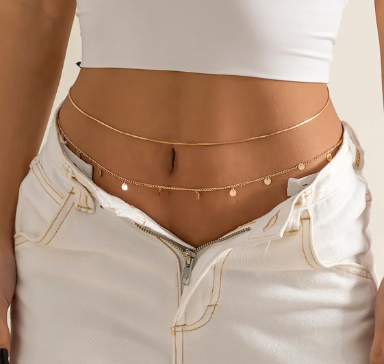Person wearing a white top and white pants with a gold chain belt.