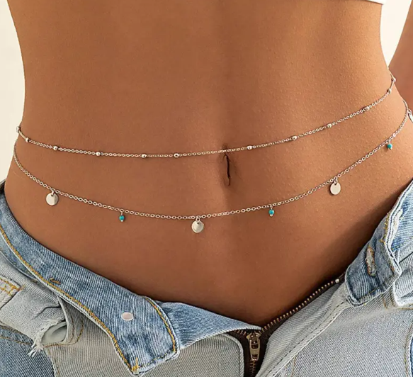 Layered chain necklaces with small pendants on a person wearing a denim jacket.